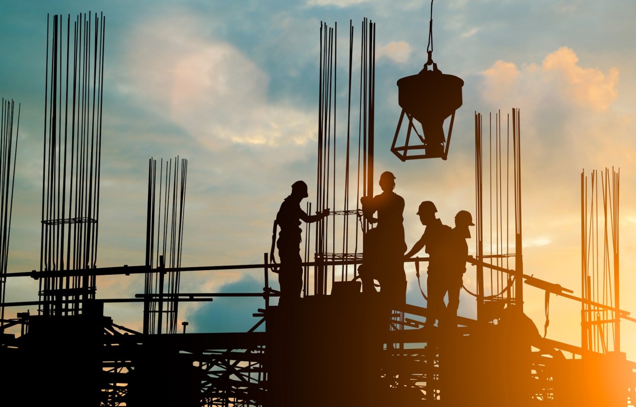 Construction workers on a site with scaffolding during sunset, silhouetted against the sky.