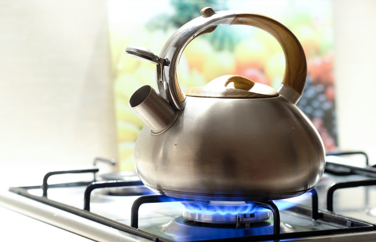 A silver kettle on a stove with flames underneath.
