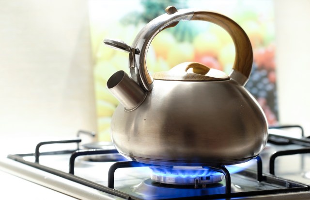 A silver kettle on a stove with flames underneath.