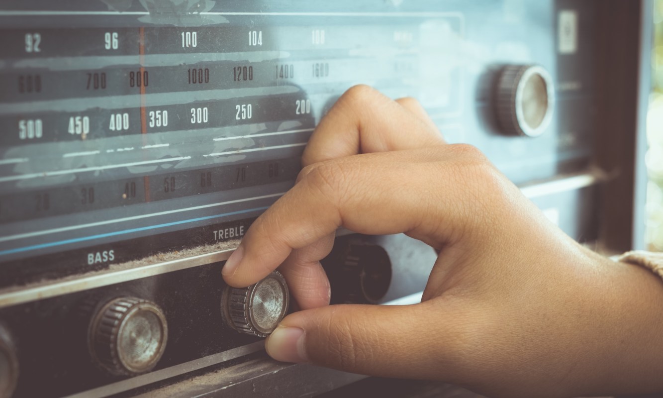 A hand adjusting the treble and bass knobs on an old radio.