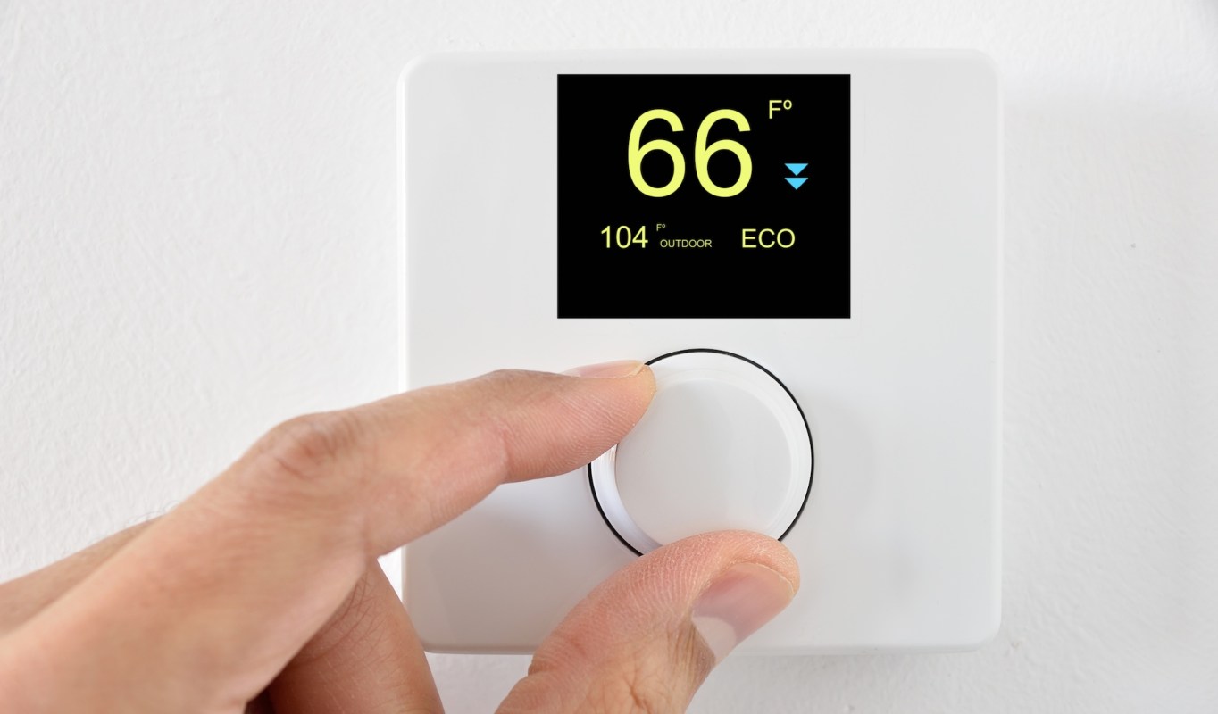 A hand adjusting a thermostat display showing 66°F and 104°F outdoor temperature.