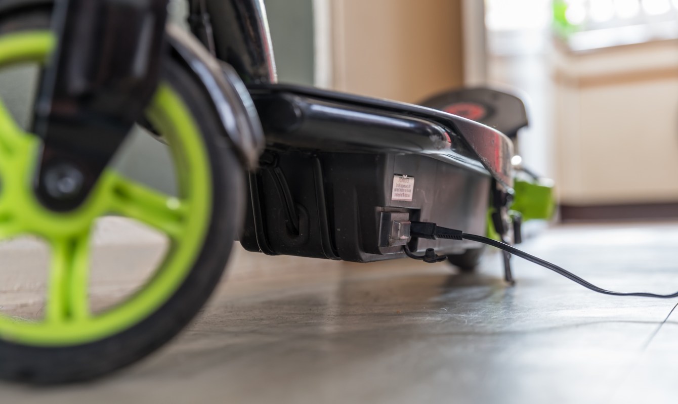 An electric scooter is plugged in for charging on a smooth surface.