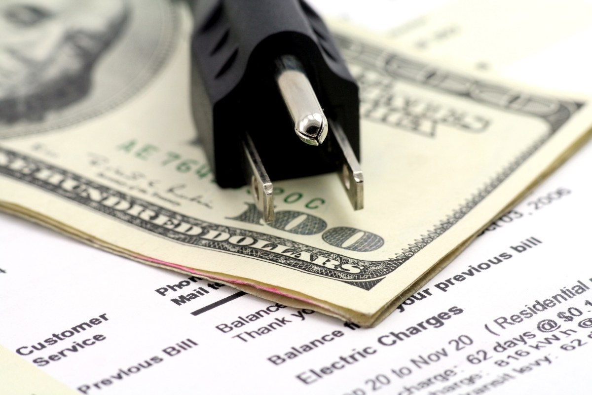 An electric plug on cash and a utility bill.