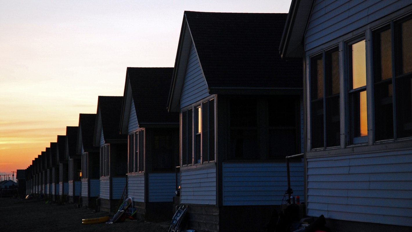 A row of beach houses at sunset, with windows reflecting orange light.