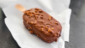 A chocolate-covered ice cream bar sprinkled with nuts on a white wrapper.