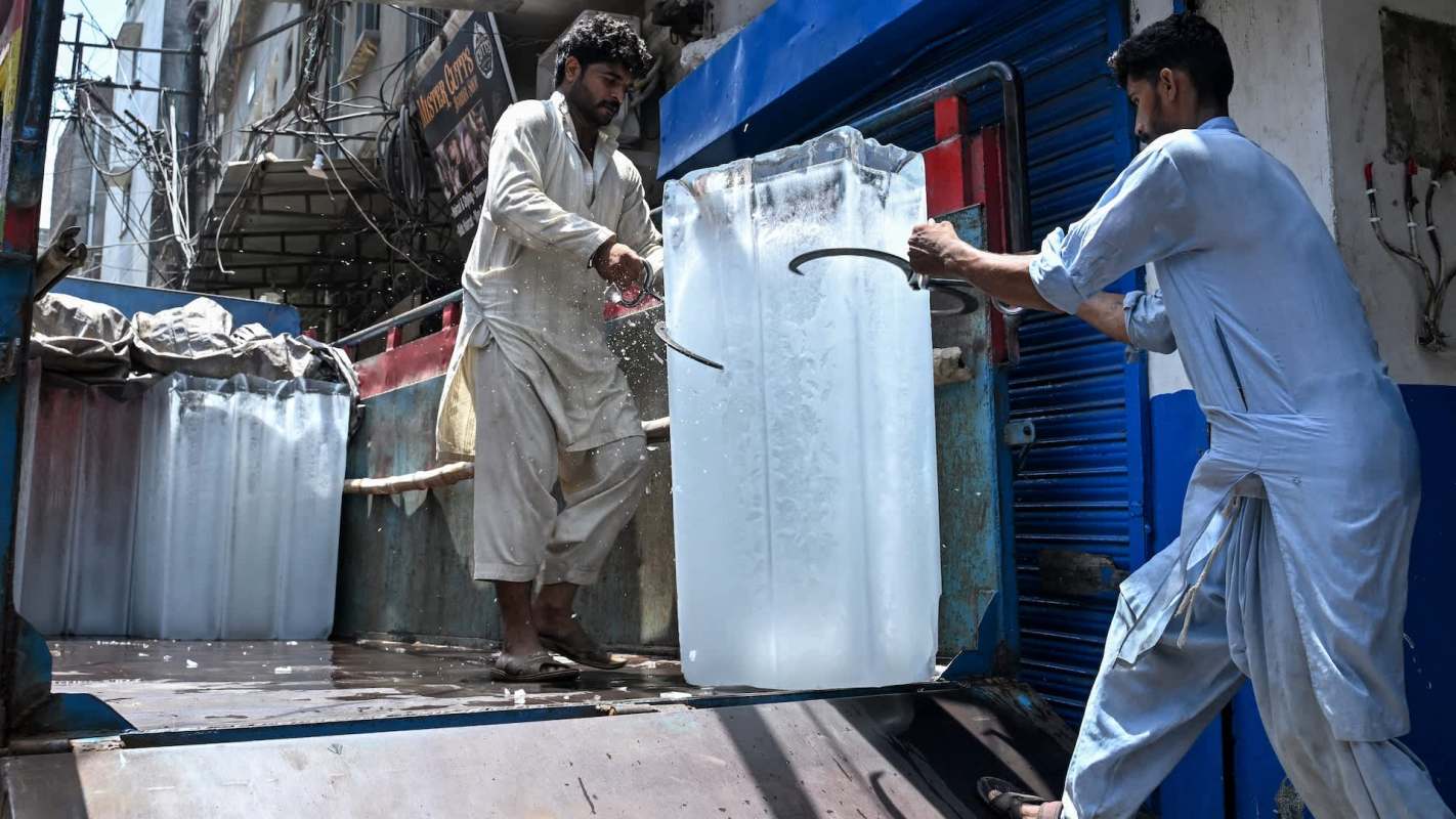 Two men unloading large blocks of ice from a truck in an urban area.