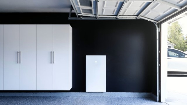 A garage with white cabinets and a wall-mounted battery system against a black wall.