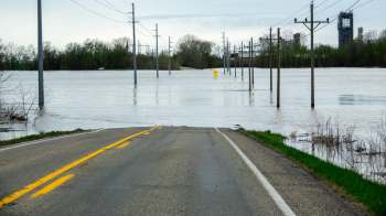 A flooded road with power poles and warning signs partially submerged in water.