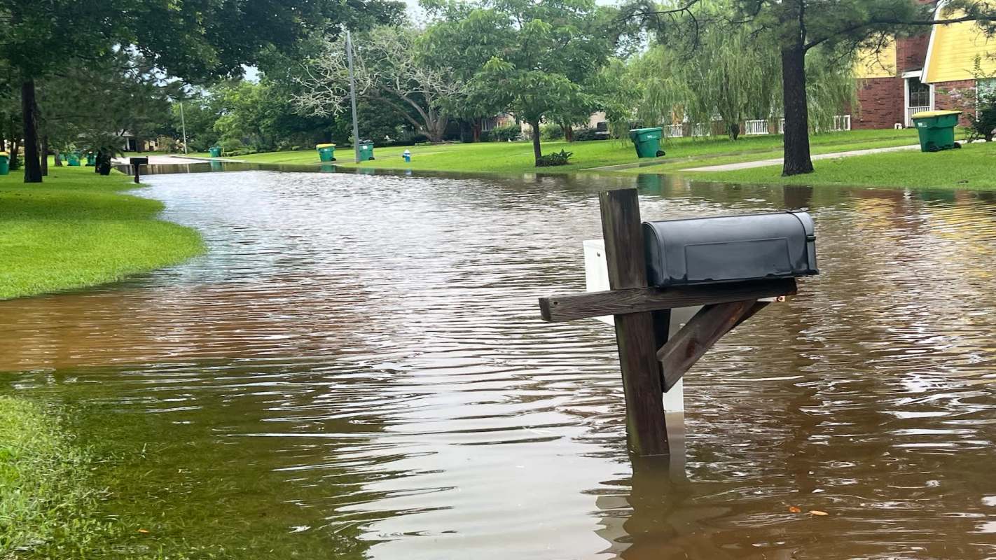 A mailbox partially submerged in floodwater on a residential street.