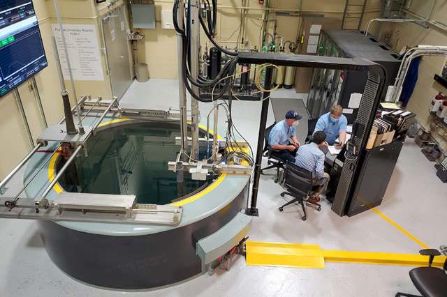 A control room with a circular reactor pool and three people discussing at a table.