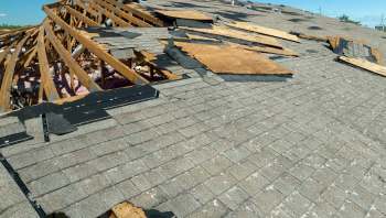 A damaged roof with missing shingles and exposed wooden beams.