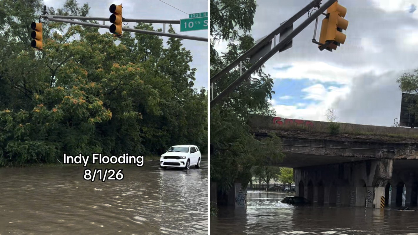 A flooded street with traffic lights, a submerged vehicle, and trees in the background.