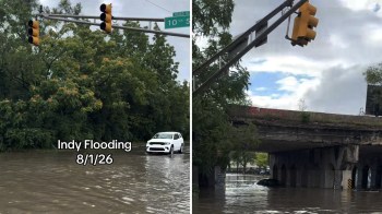 A flooded street with traffic lights, a submerged vehicle, and trees in the background.