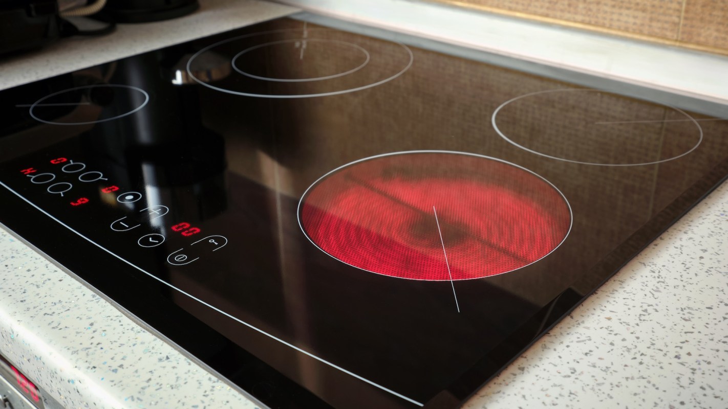 An electric cooktop with one heating element illuminated in red and control buttons displayed.