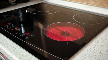 An electric cooktop with one heating element illuminated in red and control buttons displayed.