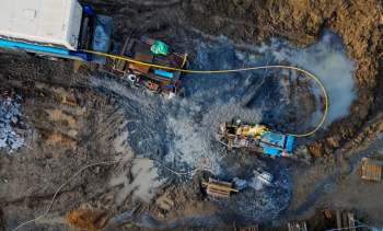Construction equipment works on a muddy site with various materials and debris scattered around.
