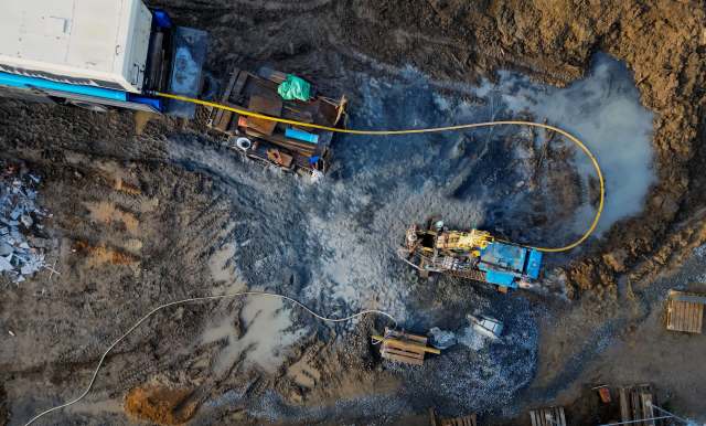 Construction equipment works on a muddy site with various materials and debris scattered around.