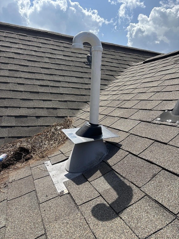 A vent pipe on a textured roof with visible debris and shadows.