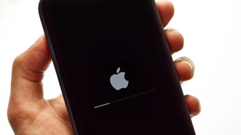 A hand holding an iPhone displaying the Apple logo and a loading progress bar.