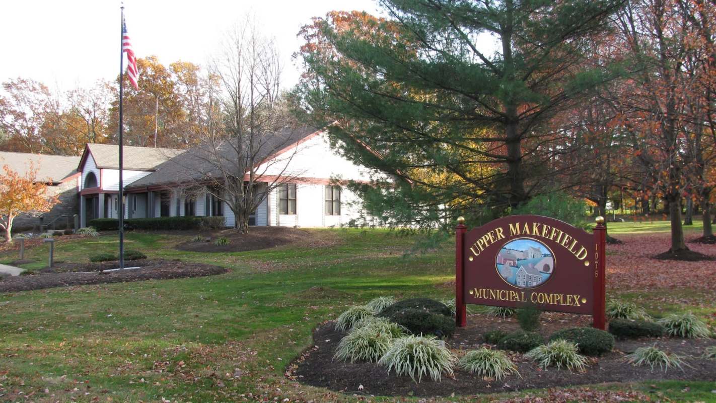A municipal complex sign in front of a building surrounded by trees and landscaped gardens.