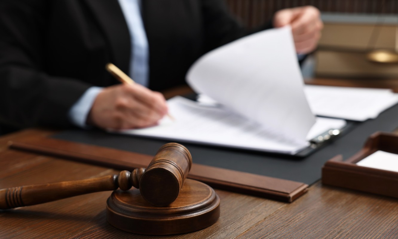 A gavel rests on a table in front of a person reviewing documents in a legal setting.