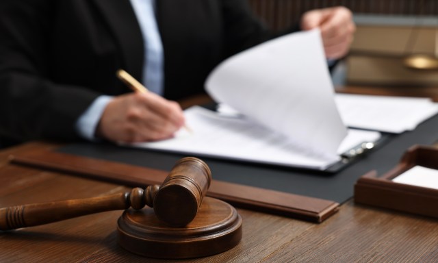 A gavel rests on a table in front of a person reviewing documents in a legal setting.
