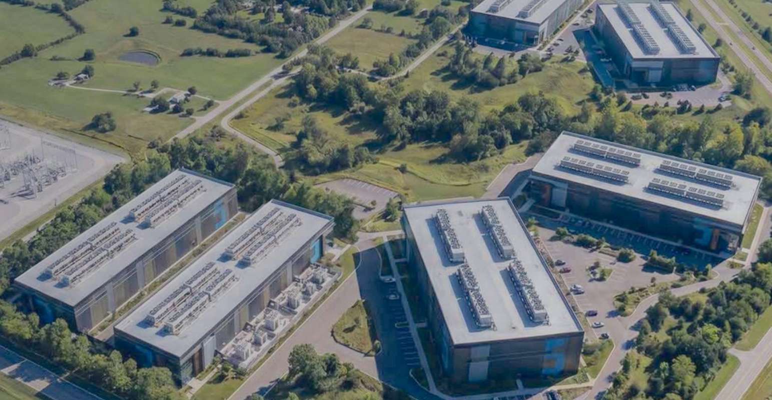 An aerial view of several data center buildings surrounded by greenery and roads.