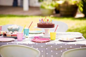 A colorful birthday cake with candles and assorted treats on a table set for a celebration outdoors.