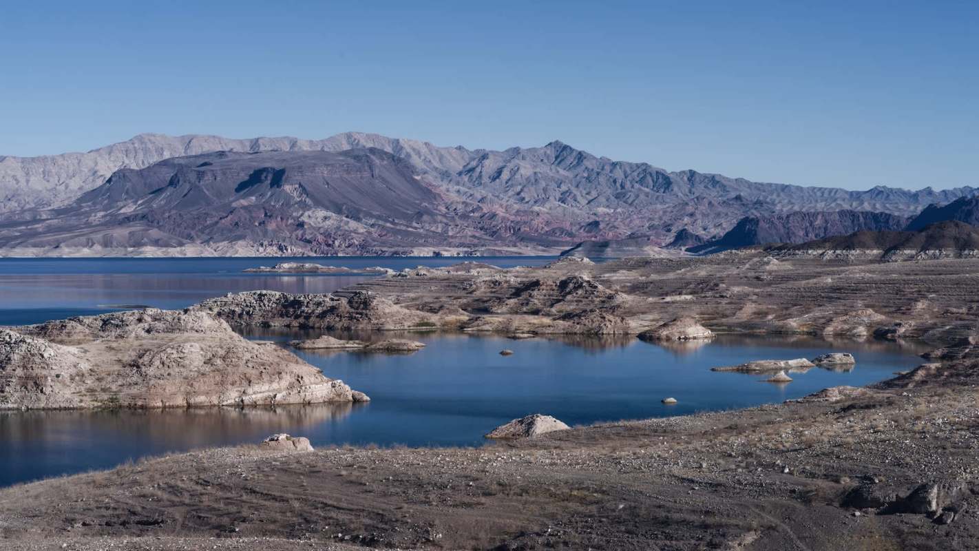 A panoramic view of a landscape with rocky formations and a low body of water surrounded by mountains.