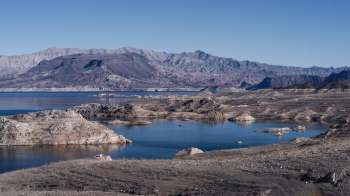 A panoramic view of a landscape with rocky formations and a low body of water surrounded by mountains.