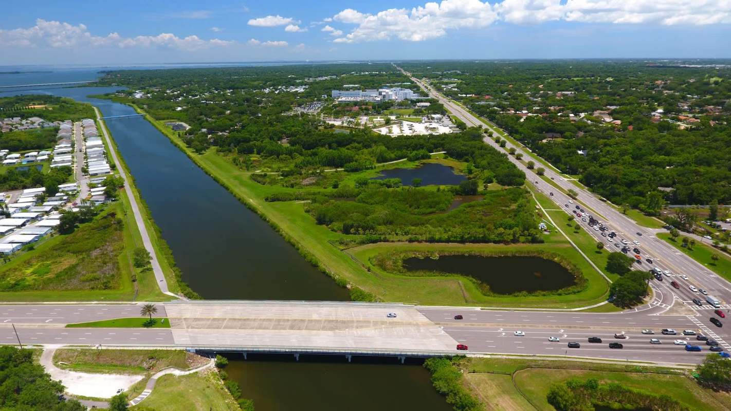 An aerial view of a highway with a river, green landscapes, and residential areas nearby.