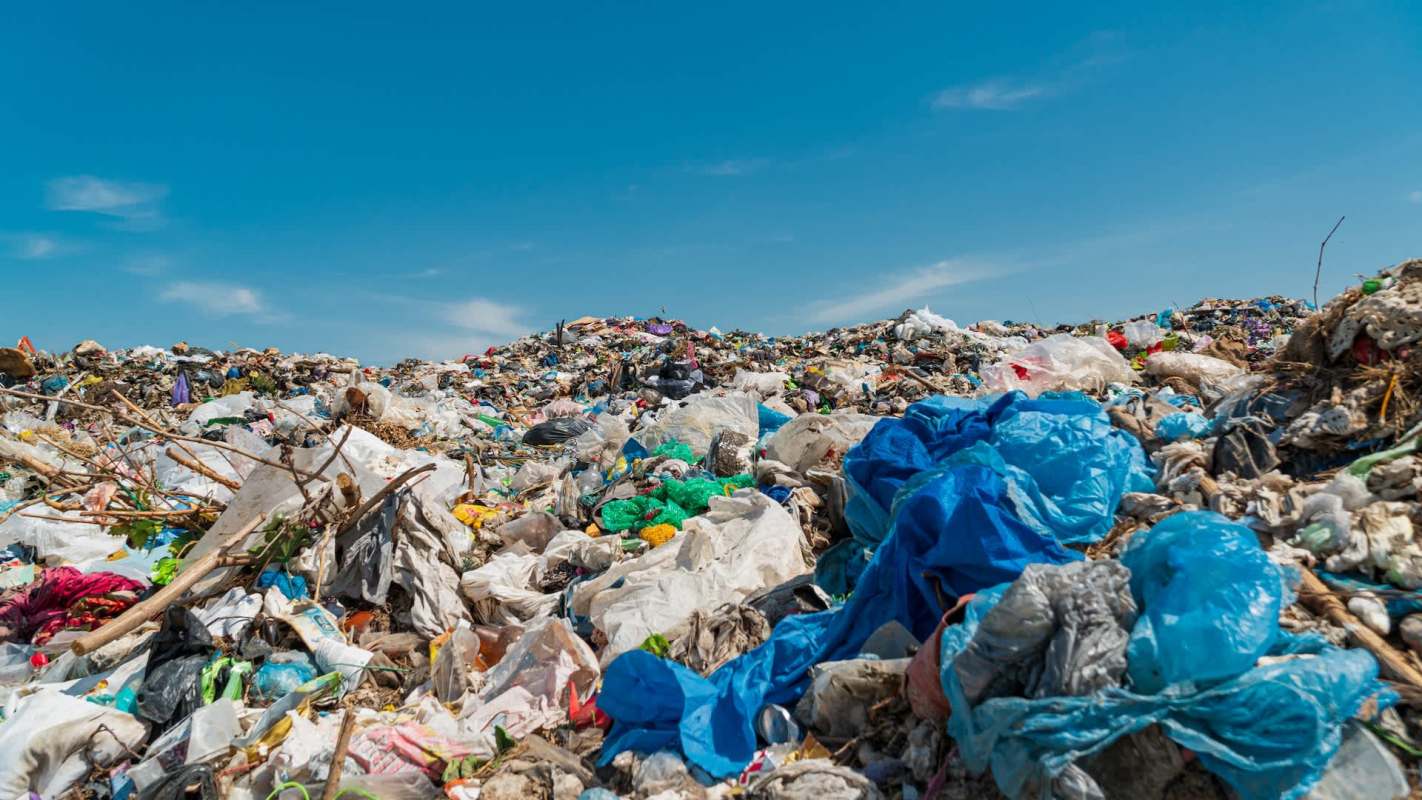 A large pile of plastic waste and garbage under a clear blue sky.