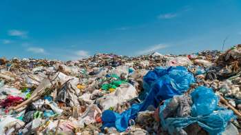 A large pile of plastic waste and garbage under a clear blue sky.