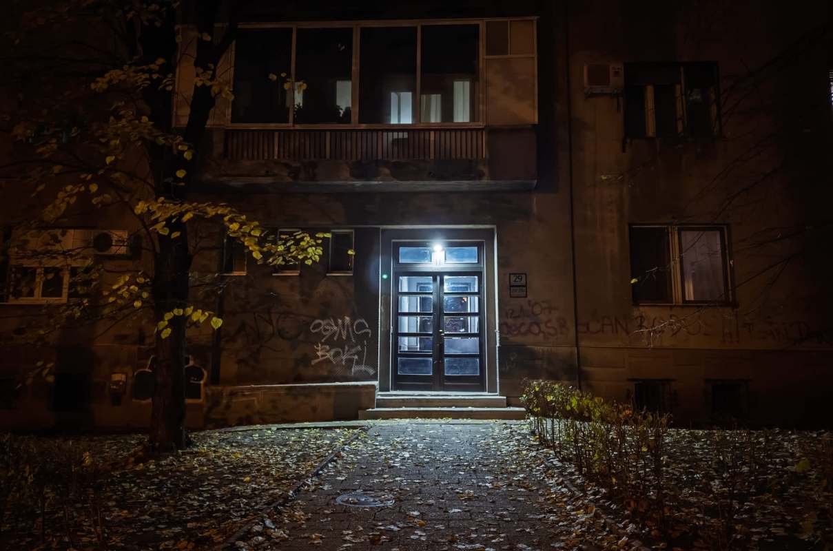 A well-lit entrance of an apartment building at night with autumn leaves scattered on the ground.