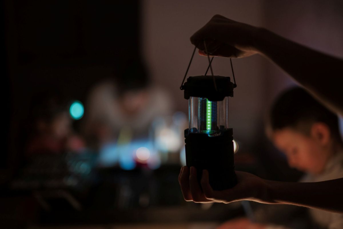 A person holding an LED lantern in a darkened room.
