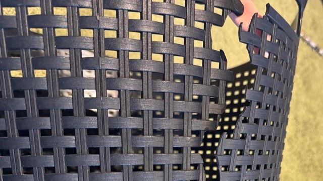 A black woven plastic basket with a visible hand holding one side.