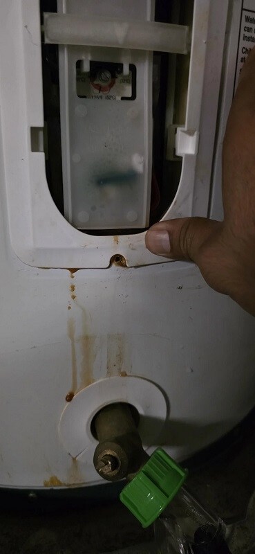A water heater leaking water on the floor in a garage.