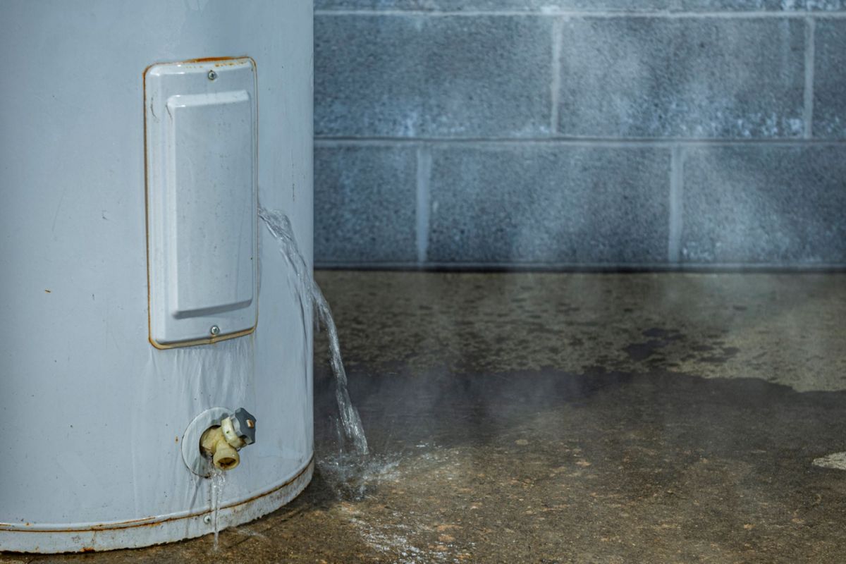 A water heater leaking water on the floor in a garage.
