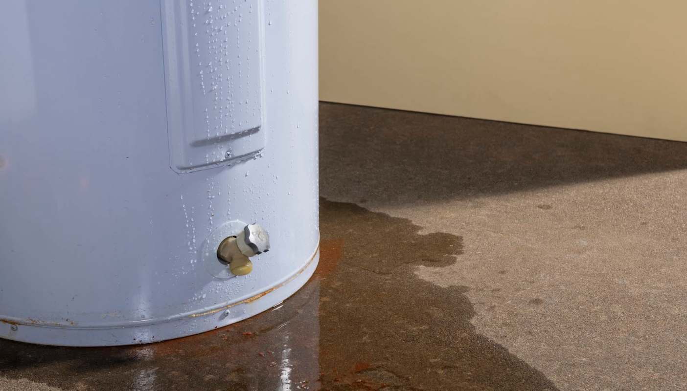A water heater with water pooling on the floor below it.