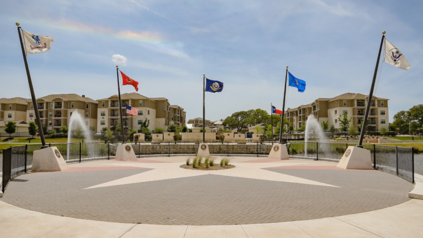 A memorial area with flags and a fountain, surrounded by residential buildings and green space.