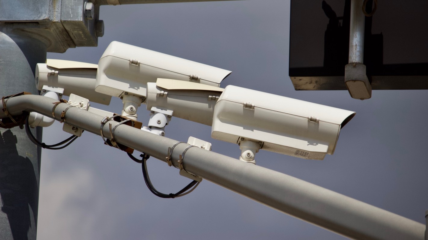 Three surveillance cameras mounted on a metal pole with visible wiring.