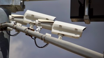 Three surveillance cameras mounted on a metal pole with visible wiring.