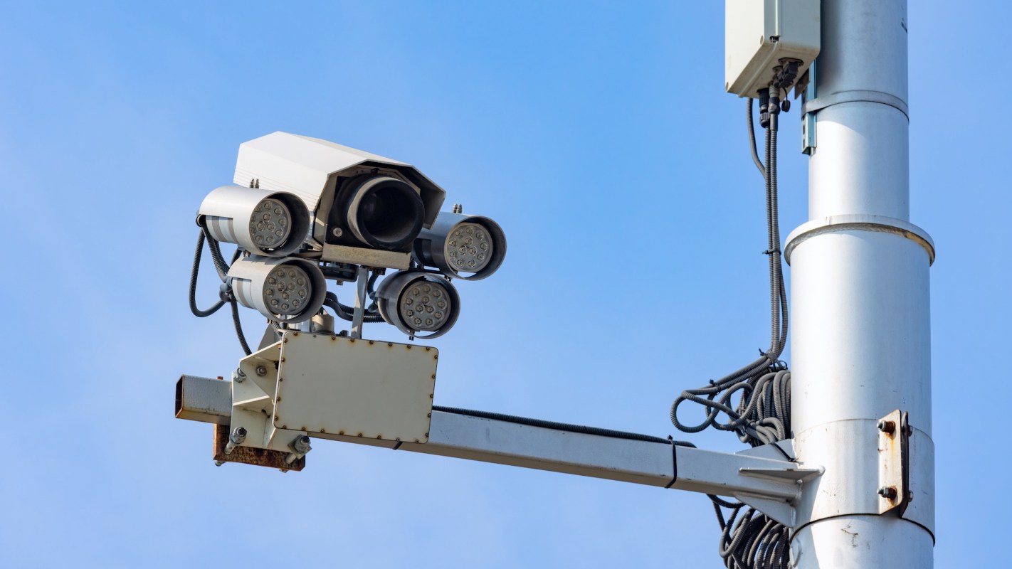 A security camera mounted on a pole with various light attachments against a clear blue sky.