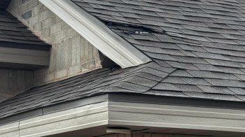 A damaged section of a roof with missing shingles and a visible gap near the ridge.