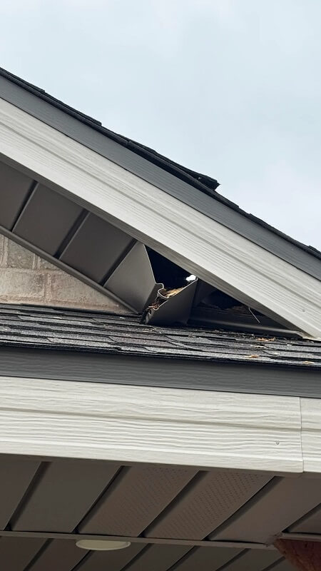 A damaged section of a roof with missing shingles and a visible gap near the ridge.