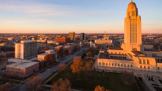 A panoramic view of a city skyline at sunset, featuring notable buildings and a prominent tower.