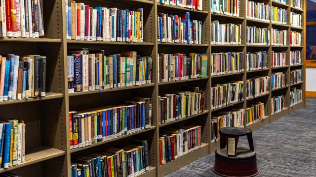 Bookshelves filled with various books and a small stool in a library setting.