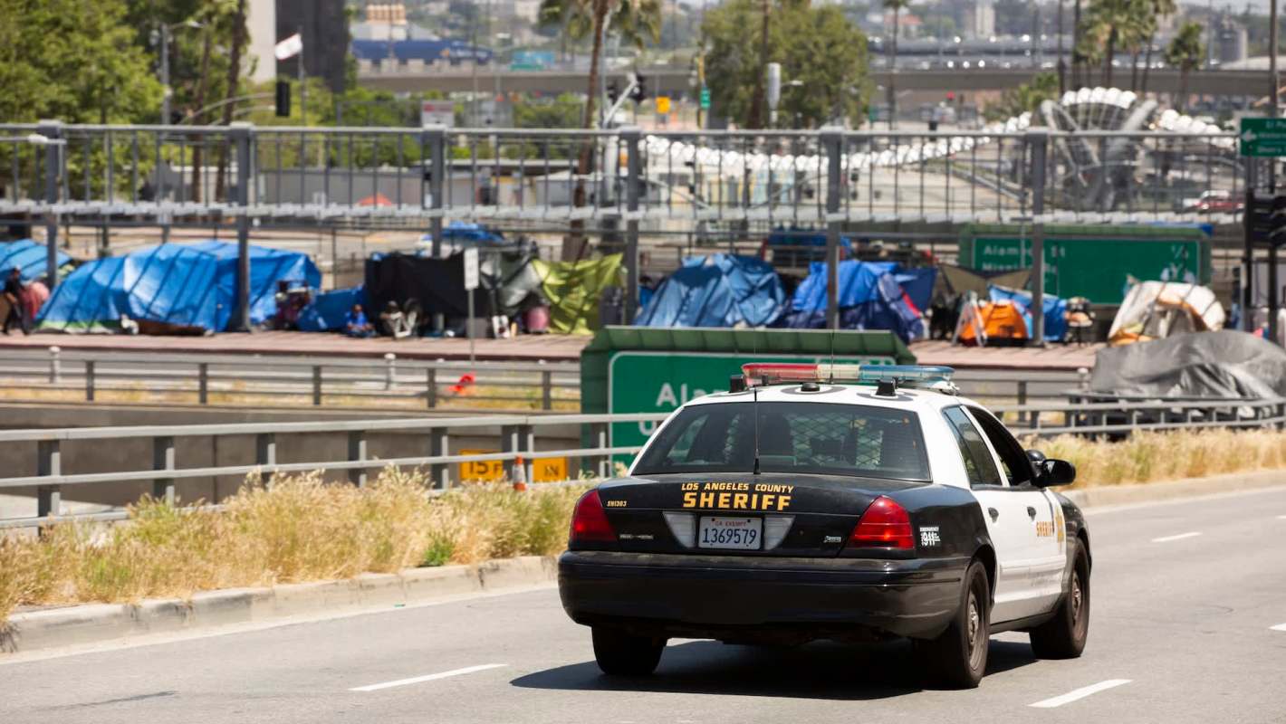 A police car driving near an encampment.