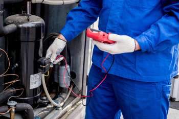 A technician tests a compressor with a multimeter while wearing gloves.