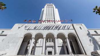 Los Angeles City Hall building with flags and palm trees in the foreground.